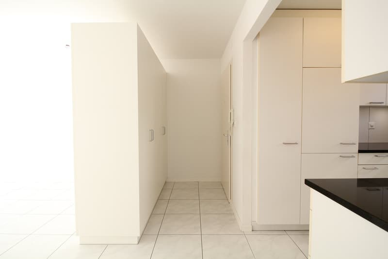 Empty hallway with white tiles, white cabinets, black countertop