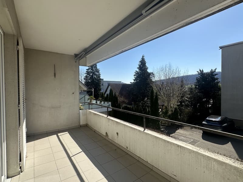 Balcony with tiled floor, metal railing, and a view of trees and a car