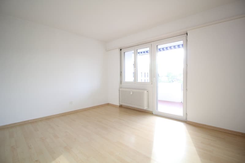 empty room, white walls, wooden floor, sliding glass door to balcony, white radiator