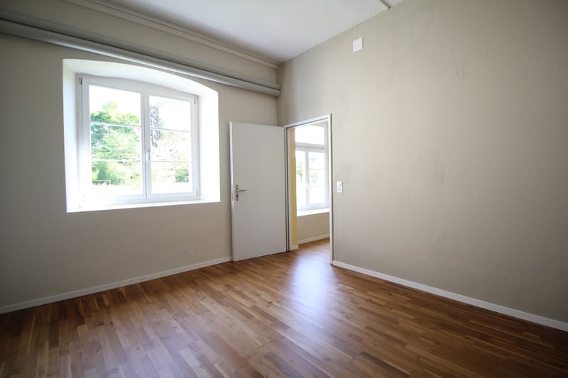 Empty room with wooden floors, white walls, and a window. No furniture or equipment.