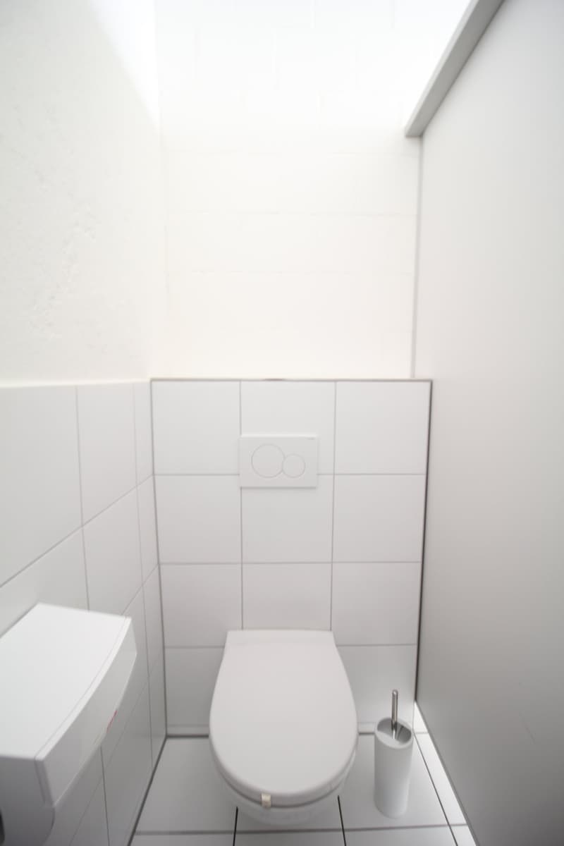 A small, white bathroom with a toilet, sink, and toilet paper holder.