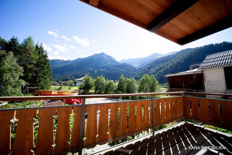 Wooden railing, clear blue sky, mountains, greenery, road with vehicles