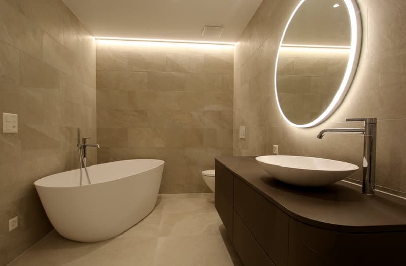 white bathtub, modern vanity, sink, oval mirror, dark tile flooring, recessed lighting, two electrical outlets