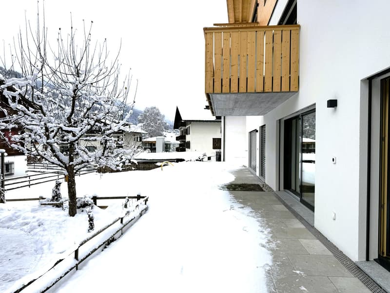 exterior of a building with wooden balcony, snow on the ground, metal fencing, trees, glass doors