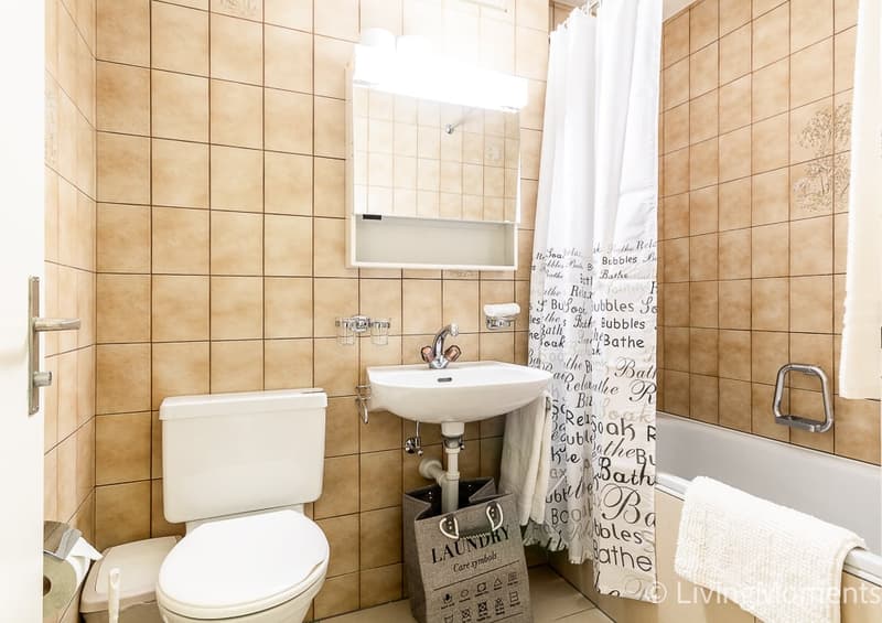 Bathroom with beige tile walls, white sink, toilet, and a laundry basket with the word 'Laundry' written on it.