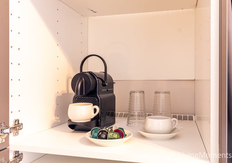 Small kitchen nook with a coffee machine, cups, and a bowl of coffee capsules