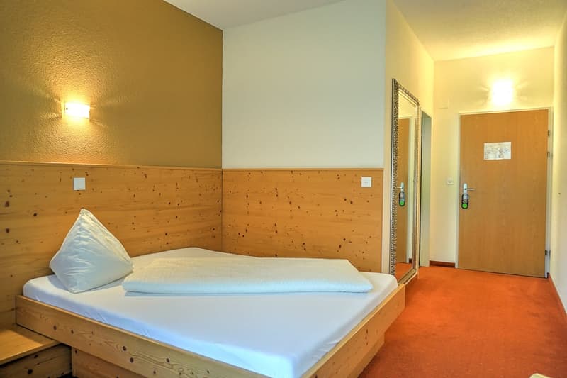 Wooden paneled walls, double bed with white bedding, wooden furniture, hallway visible through open door