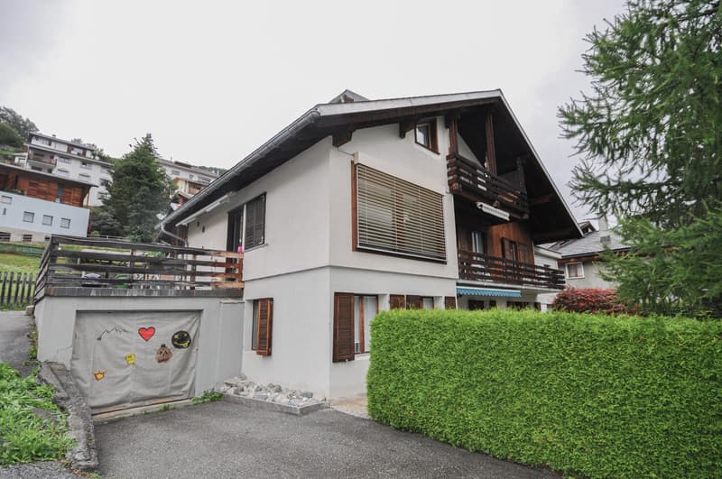 two story house, wooden balcony, garage with decorations, white walls, gray roof, window shutters, greenery around
