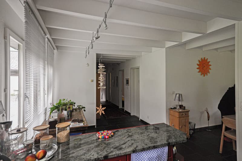 room with marble countertop, large white exposed beams, lamp, sun clock, plants on a table, and open corridor with wooden flooring