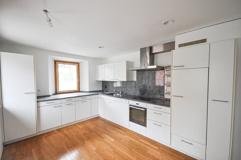 Spacious L-shaped kitchen with white cabinets, granite countertops, stainless steel appliances including a dishwasher, and a large window providing natural light. The kitchen has a hardwood floor and an open layout.