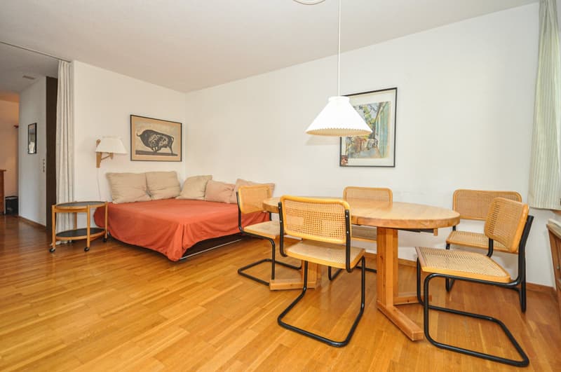 A room with a bed, couch, table and chairs.