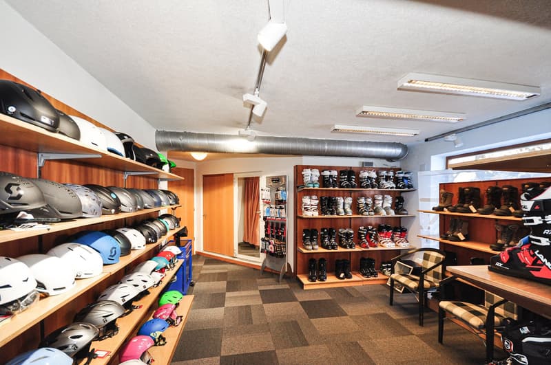 Carpeted floor, numerous shelves with ski gear, helmets displayed, shelves with ski boots, chair