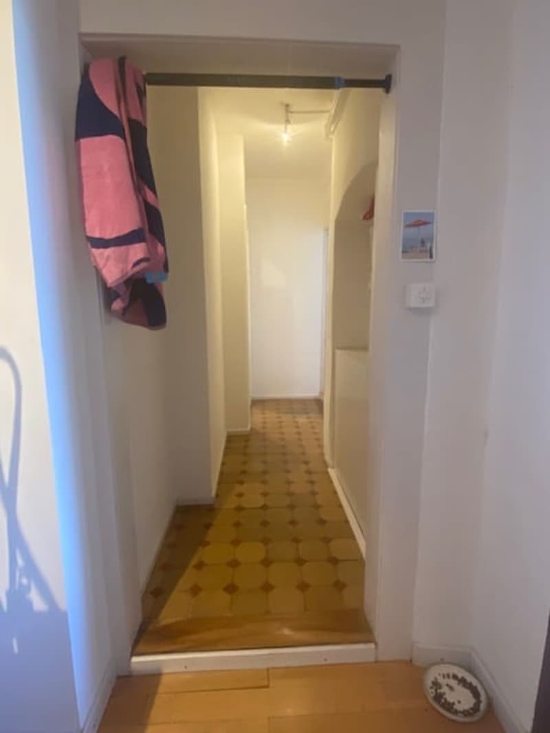 Empty hallway with tiled floor, white walls, door, picture frame, towel, and light fixture.