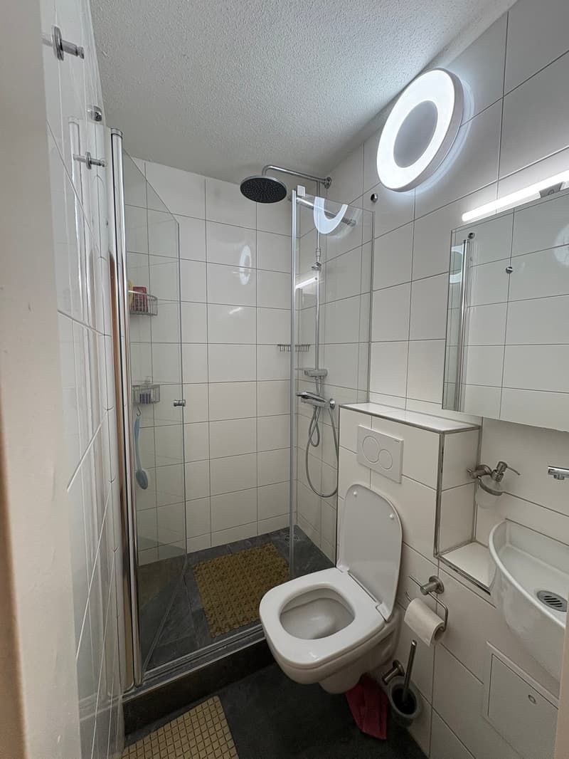 white tiled bathroom with toilet, shower, sink, and shower cabin