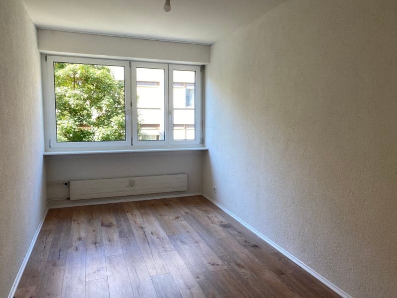 Empty room with wooden floor, white walls, large window, under-window heater
