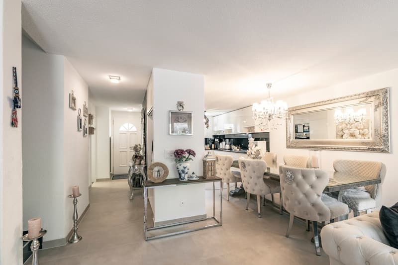 Open concept living room and kitchen, white walls, hardwood floors, tufted dining chairs, mirrored console table, chandelier, kitchen appliances