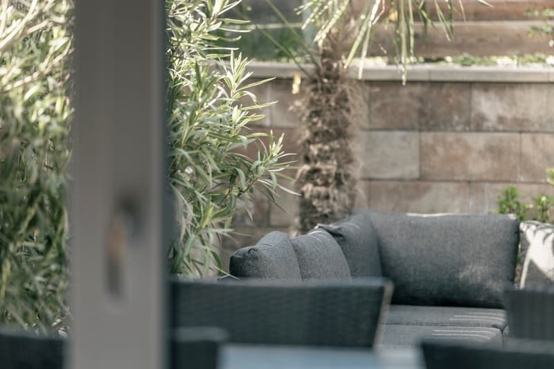 Cozy outdoor seating area with cushioned benches, surrounded by lush greenery and plants.
