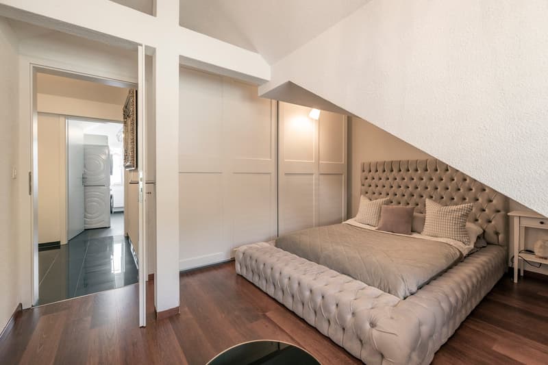 Spacious bedroom with a tufted upholstered bed, built-in closets, hardwood flooring, and an open doorway leading to a laundry area.