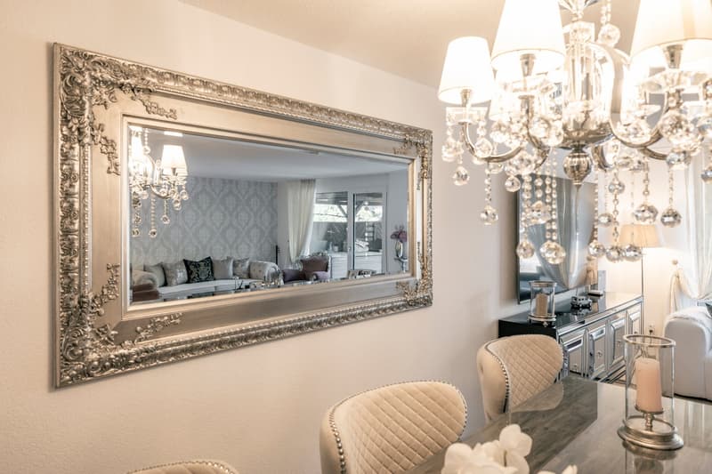 Elegant living room with a large ornate mirror, crystal chandelier, patterned curtains, plush seating, and a fireplace