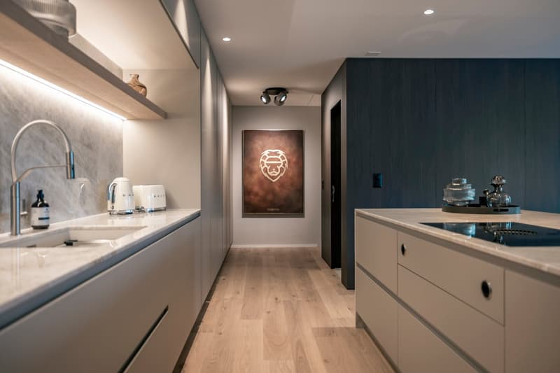 Modern kitchen with white cabinets, wooden floors, and a large artwork on the wall. The kitchen features a dishwasher and other appliances.