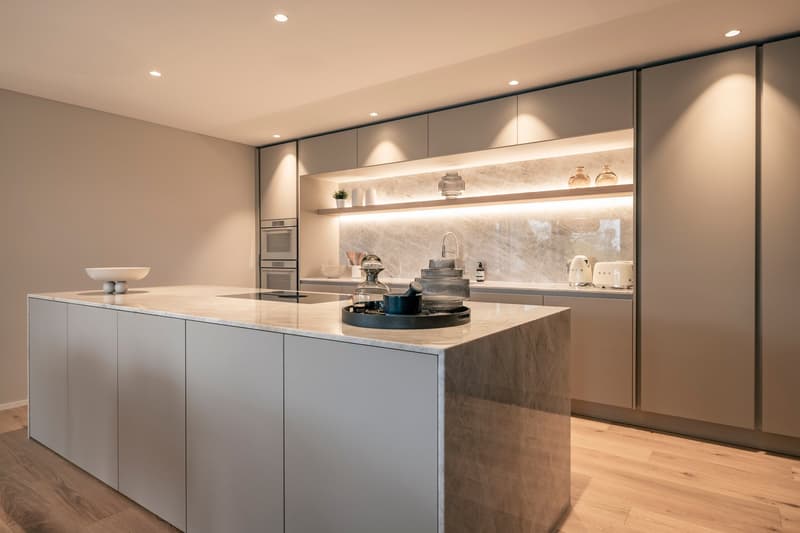 Modern kitchen with gray cabinets, marble countertops, built-in appliances, and open shelving displaying decorative items