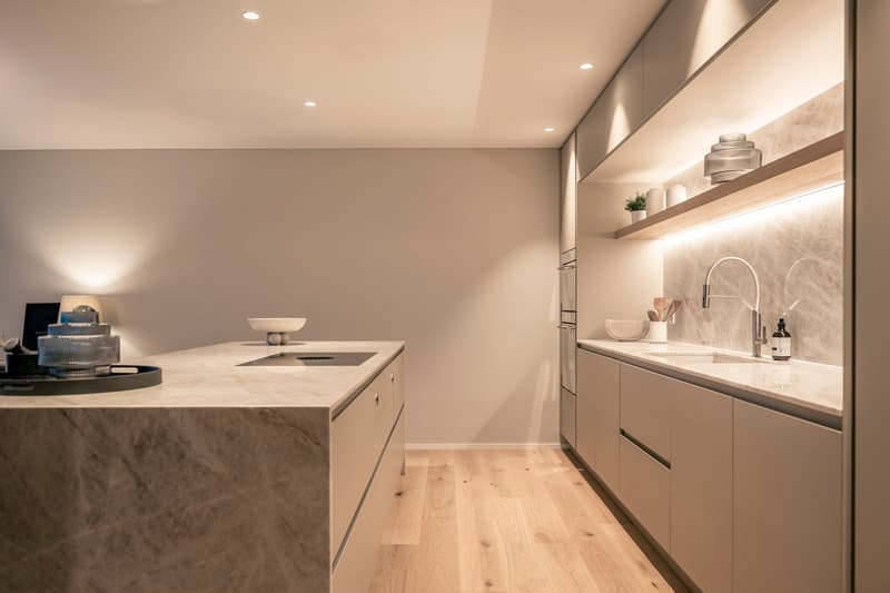Modern kitchen with light-colored cabinets, marble countertops, built-in appliances, and shelving for decor items
