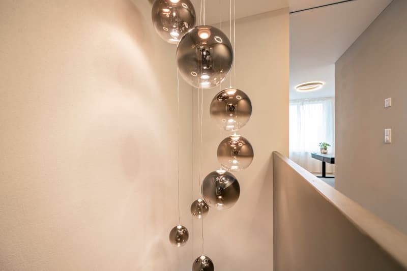 Hallway with a vertical arrangement of chrome pendant lights, white walls, and a glimpse of an adjacent room.
