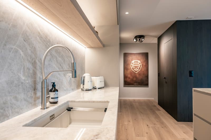 Modern kitchen with white marble countertop, stainless steel sink and faucet, built-in appliances including a dishwasher, and a framed artwork on the wall