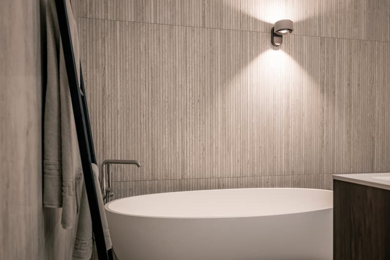 Modern bathroom with a freestanding bathtub, wooden wall tiles, and a wall-mounted light fixture.