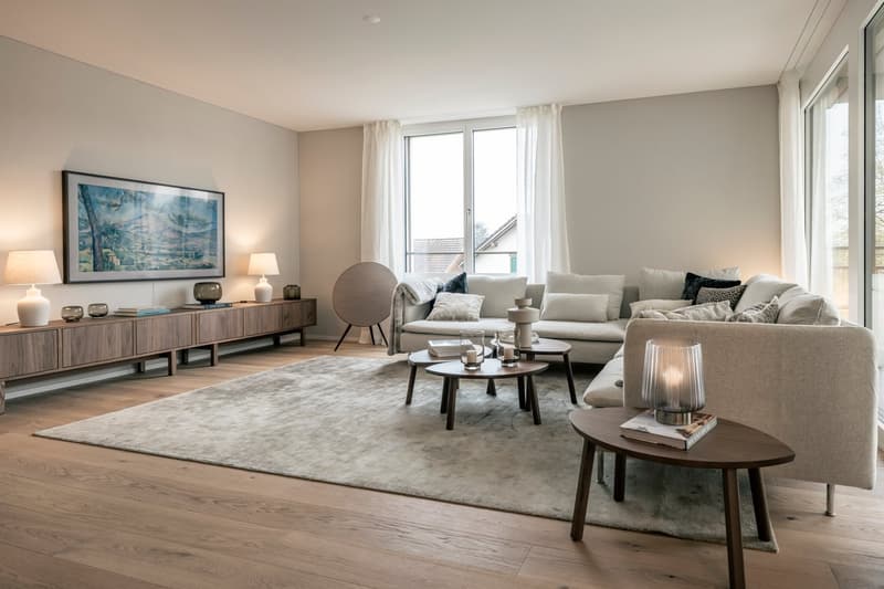 Spacious living room with large windows, hardwood floors, neutral-colored furniture including a sectional sofa, coffee table, and side tables, a media console with decor, and a large framed artwork on the wall.