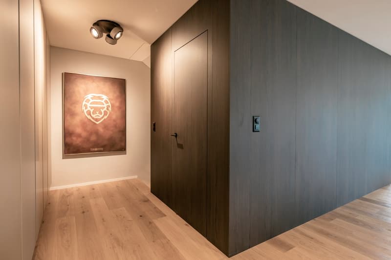 Wooden flooring, dark gray walls, recessed lighting, framed artwork on the wall, and a closed door leading to another room.