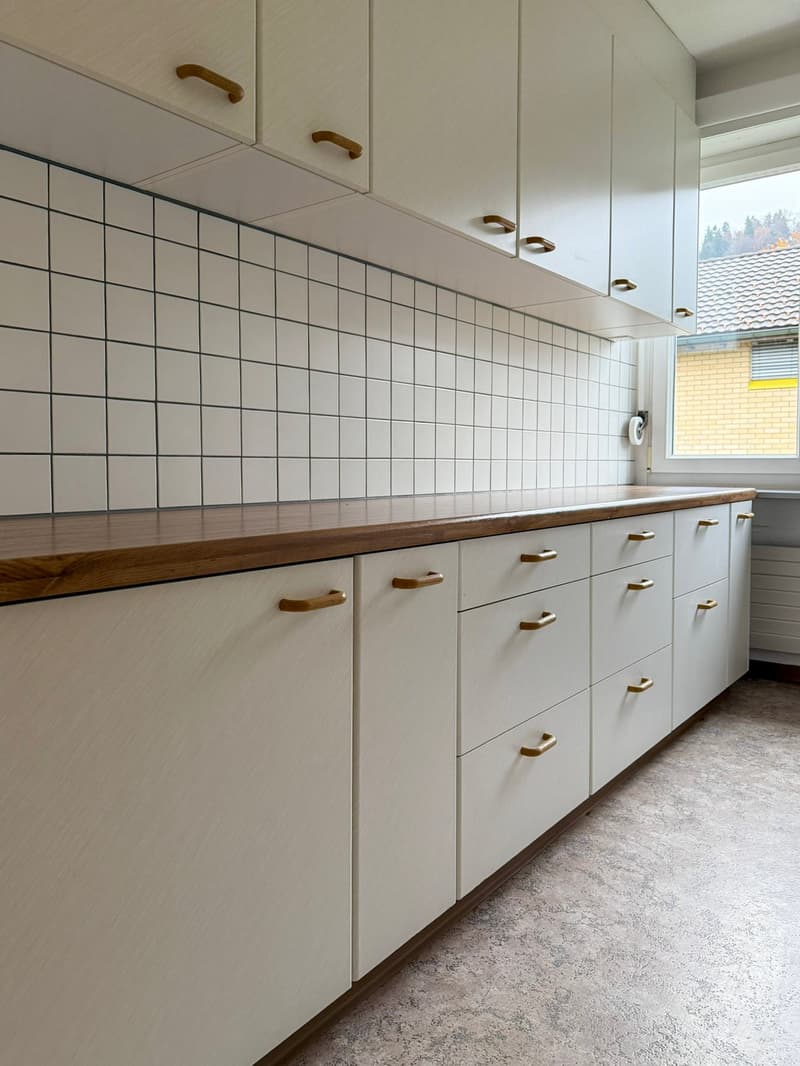 white cabinets, wooden countertop, tiled backsplash, window, brass drawer pulls