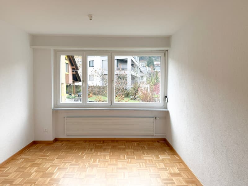 empty room with white walls, wooden floor, large window, view to outside