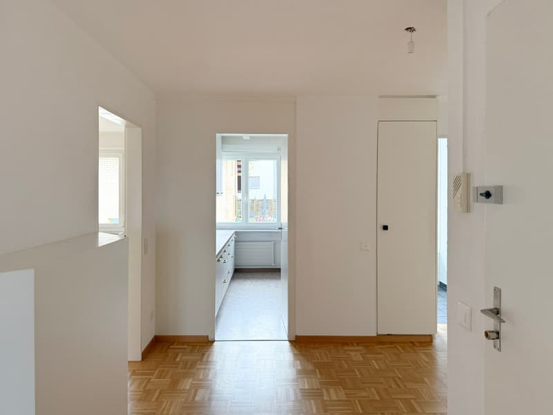 Empty room with wooden floors, white walls, two doors, a window and bright lighting.