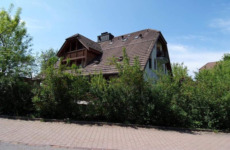 2 story house, brown roof, wooden balcony, brick wall, surrounded by bushes