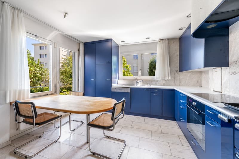modern kitchen, wooden table, blue cabinets, white countertop, large window, view of outside