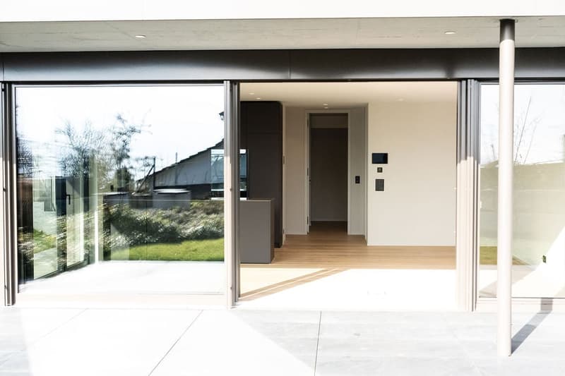 Aerial view of entrance area, glass doors, wooden floors, and patio, leading to an indoor hallway.