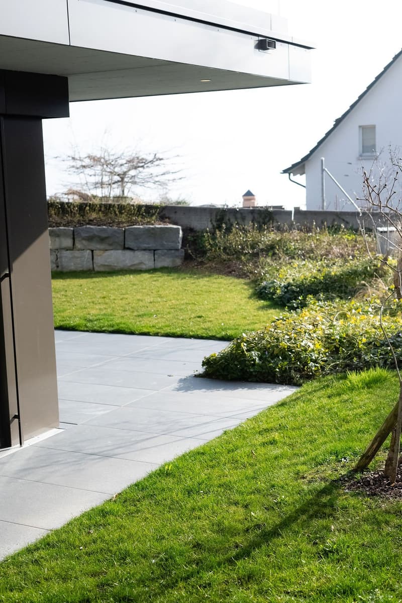 modern exterior with concrete sidewalk, concrete driveway, lawn area, stone retaining wall, no visible entrance