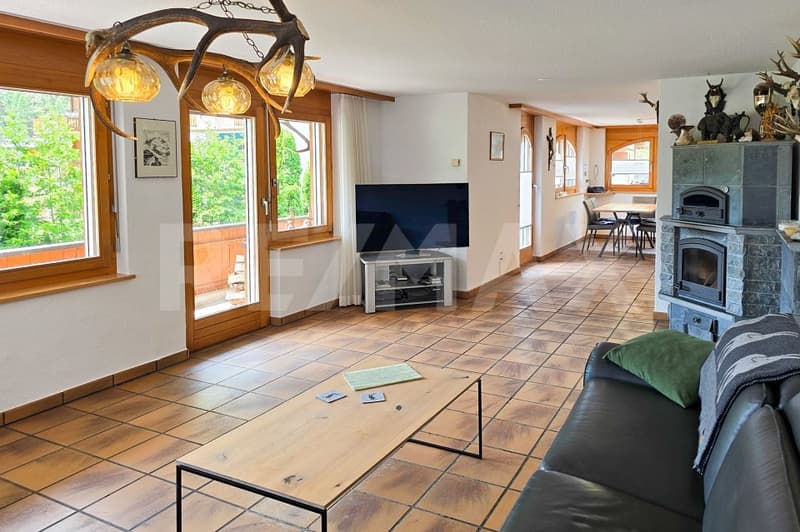 Fireplace, large windows, TV, wooden coffee table, black leather couch, tiled floor