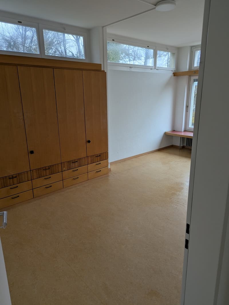 Empty room with wooden wardrobe, white walls, wooden floor, windows, small table