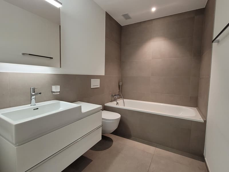 Modern bathroom with white sink, bathtub, toilet, and mirror, with tiled walls.