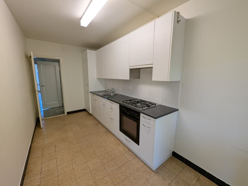 Empty kitchen with white cabinets, tiled floor, gas stove, sink, and a door leading to another room