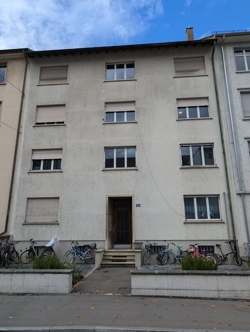 4 story building, concrete exterior, multiple windows, entrance with steps, bicycles parked in front
