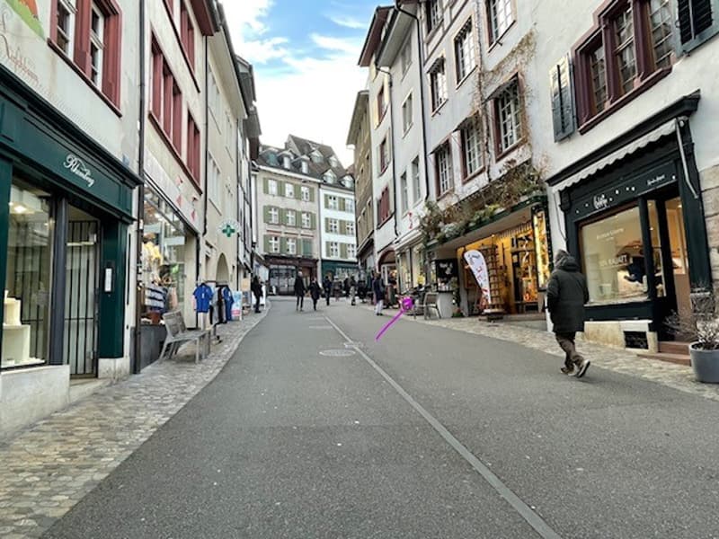 Shops on both sides, few people, cobble stone pavement on both sides, one lane road