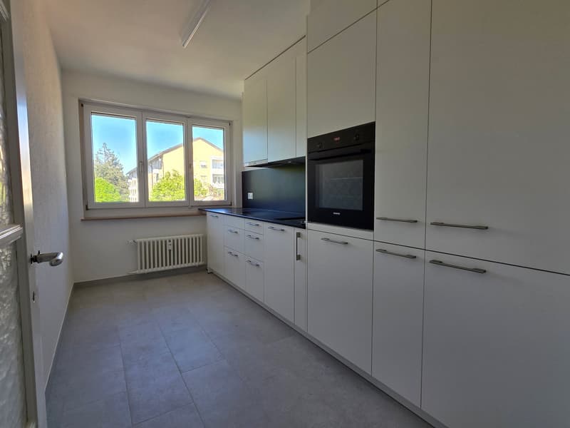 modern kitchen, white cabinets, black oven, window, tiled floor, radiator