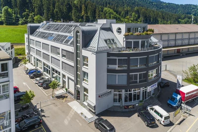 white multistory building, grey roof, several windows, parking lot, multiple solar panels