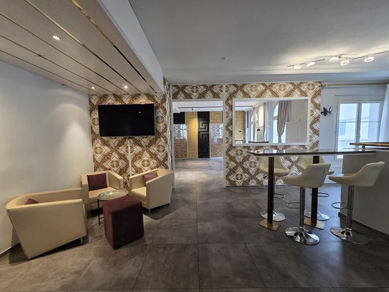 modern interior, beige walls, patterned wallpaper, beige chairs, round table, flat screen TV, bar counter, bar stools