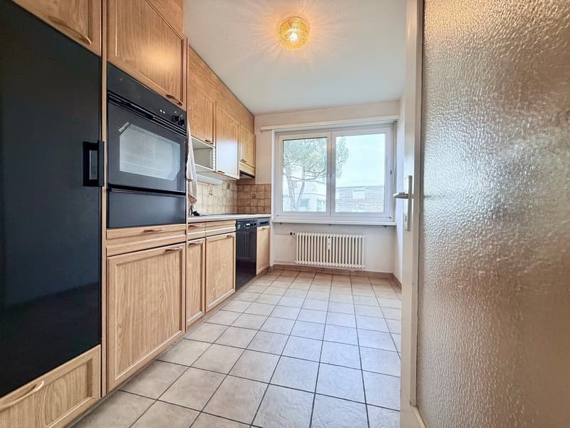 modern kitchen with wooden cabinets, black appliances, tiled floor, large window
