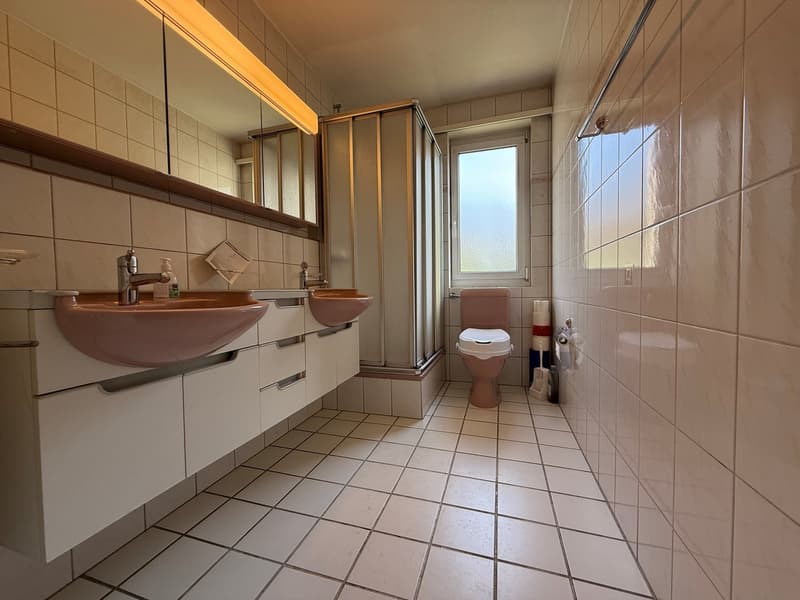 Bathroom with two sinks, a toilet, a shower, and tiled walls and floor.