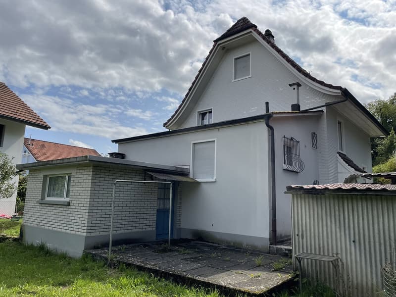 Single-family house with brick walls, tiled roof, red roof tiles, white windows, blue entrance door, gray driveway, small metal shed